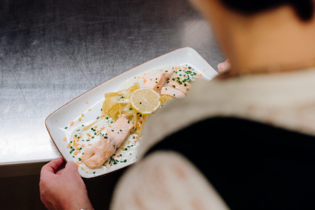 Servicekraft mit einem Teller mit Lachsnudeln