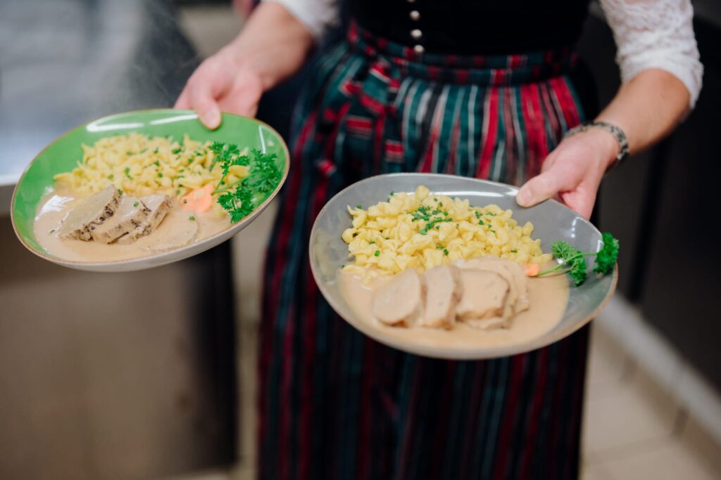 Bedienung serviert zwei Teller mit Schweinemedaillons und Spätzle