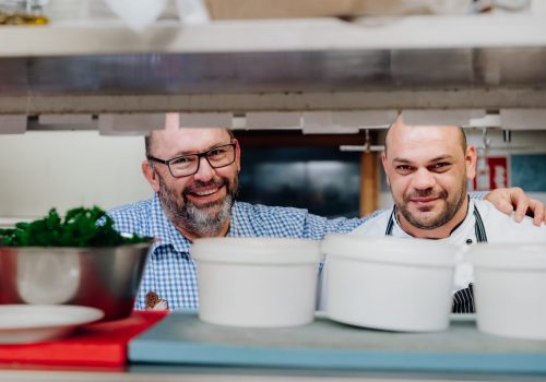 Zwei Männer stehen in der Küche und lächeln in die Kamera